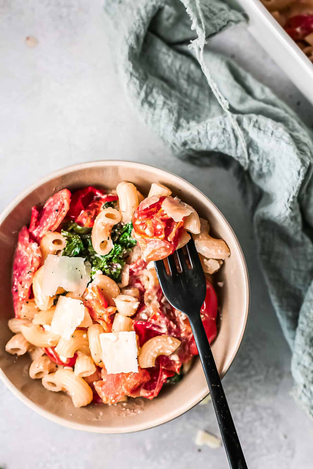 a bowl of cheesy pasta with tomatoes and kale with some on a fork