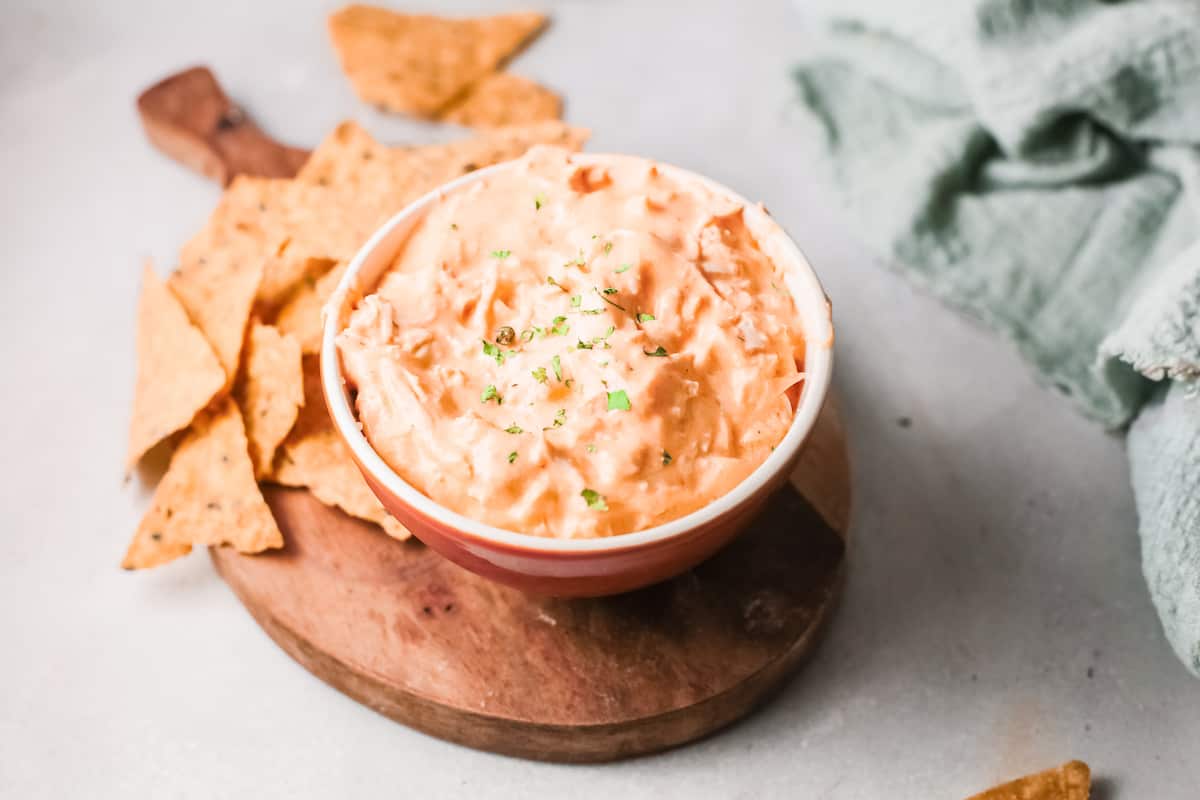 the finished instant pot buffalo chicken dip served in a bowl placed on a wooden cutting board with a handful of chips