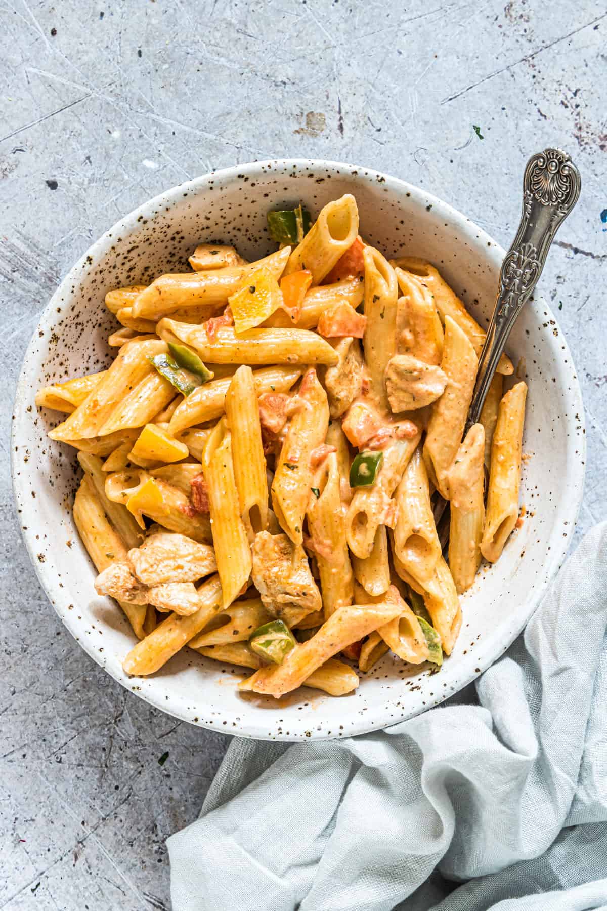 a bowl full of one pot chicken fajita pasta on a table with a fork and napkin