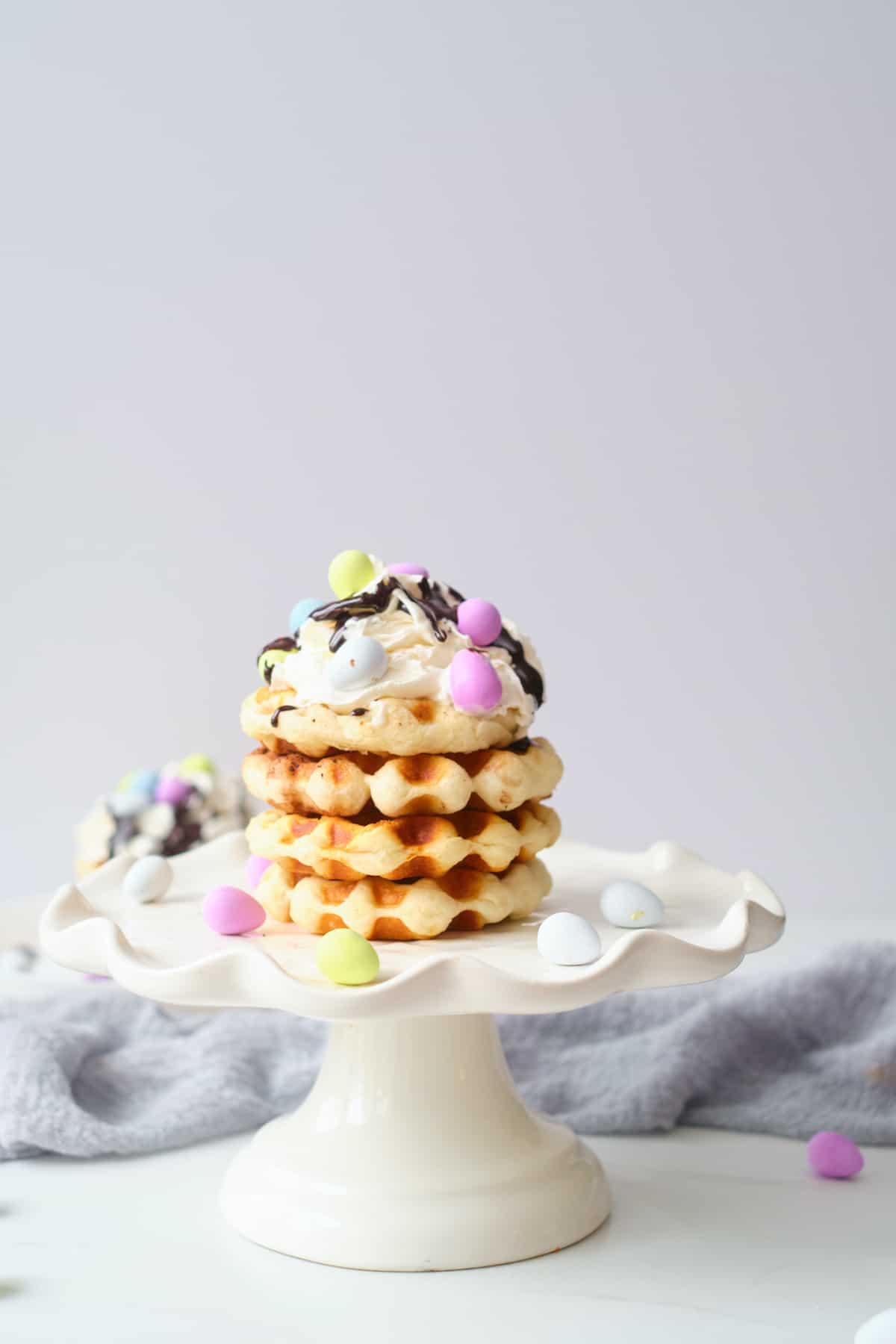 side view of 3 of the biscuit waffles stacked on a white cake stand
