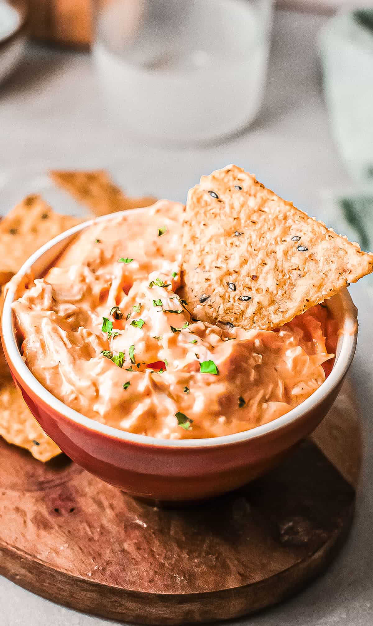 the completed instant pot buffalo chicken dip served in a red bowl with one chip dipped into it.
