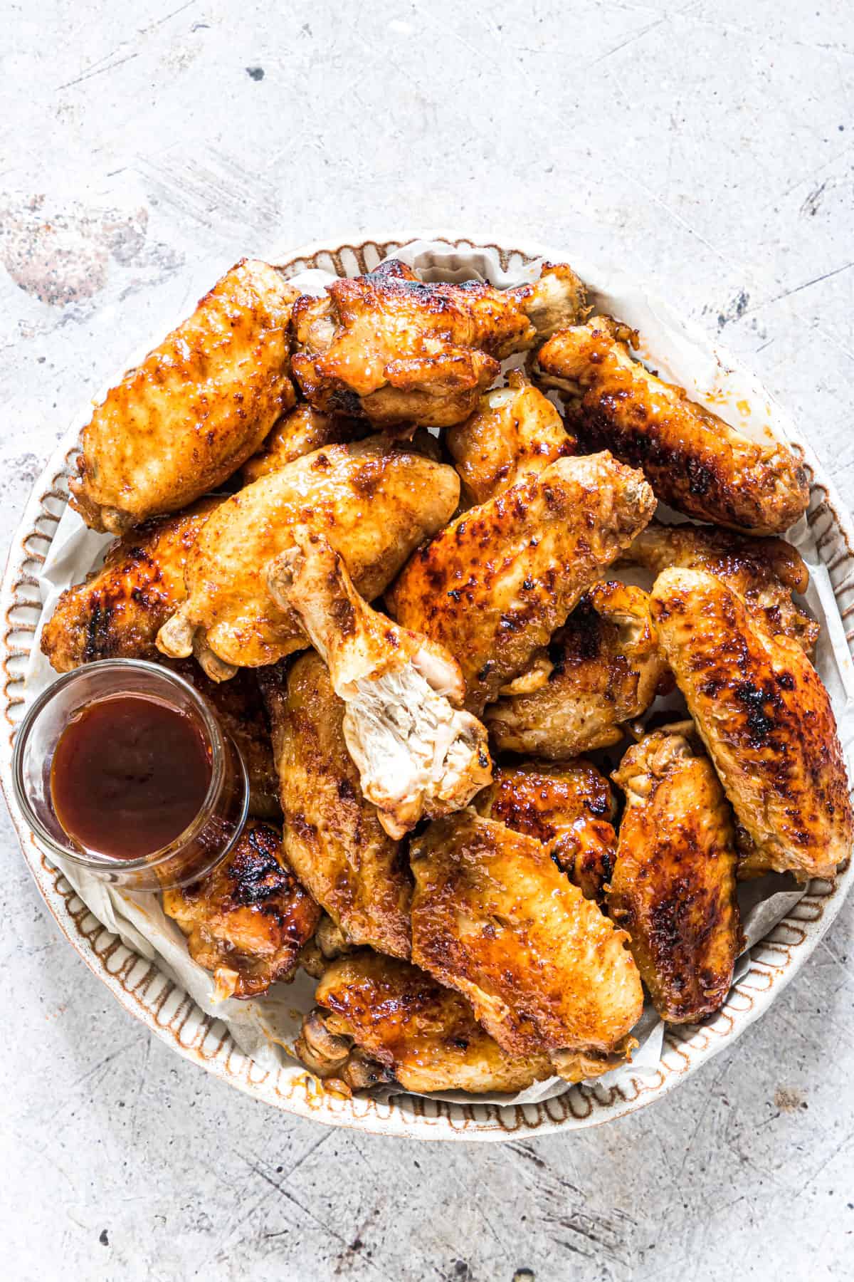 a plate filled with the completed coca cola chicken wings and served with a cup of sauce for dipping