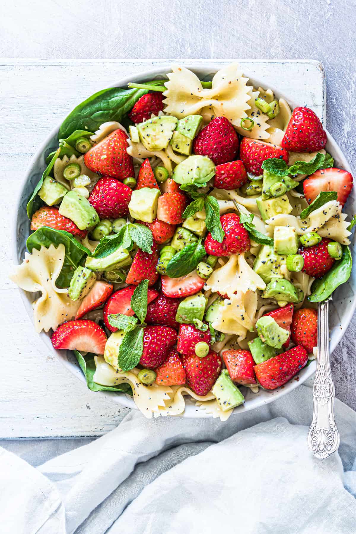 a serving of strawberry avocado salad with a fork and cloth napkin 