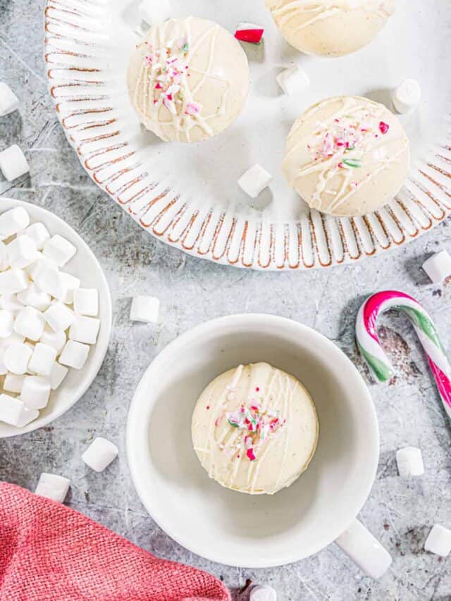 top down view of peppermint hot chocolate bomb in a white mug with the others on a plate sitting next to candy canes and a bowl of marshmallows