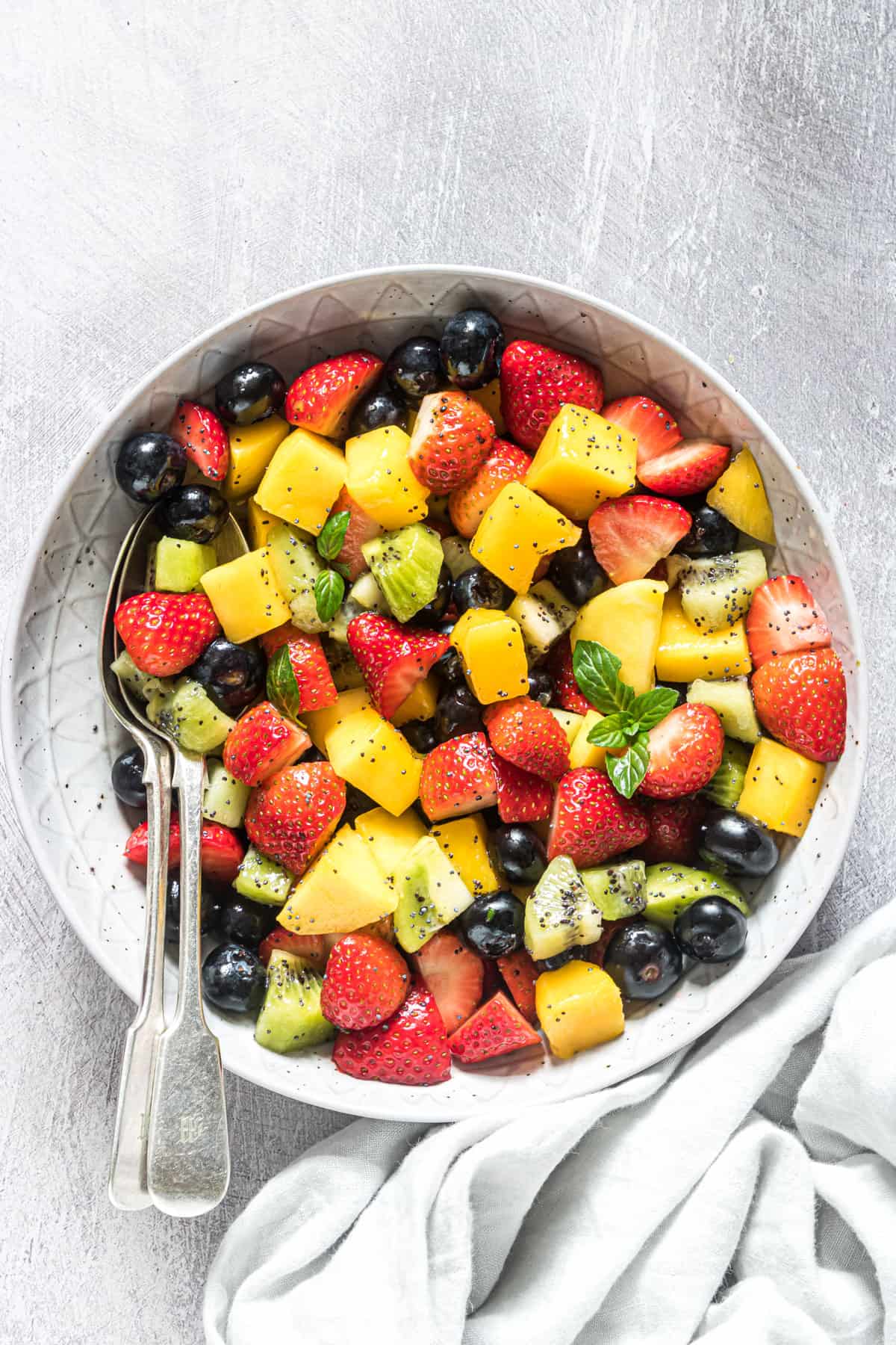 top down view of the completed fruit salad with serving utensils and cloth napkin