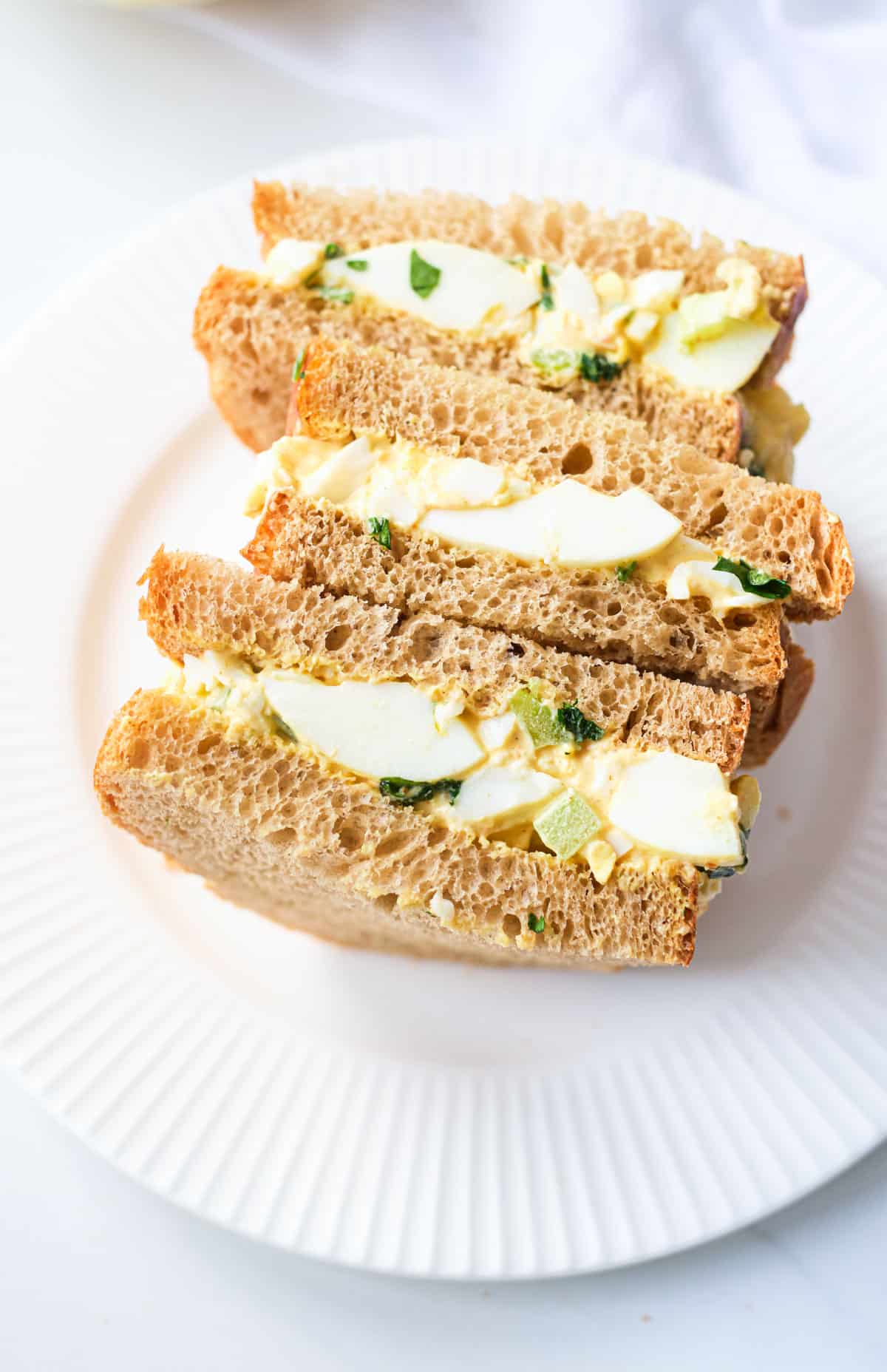 the completed egg salad sandwich cut in half and served on a white plate