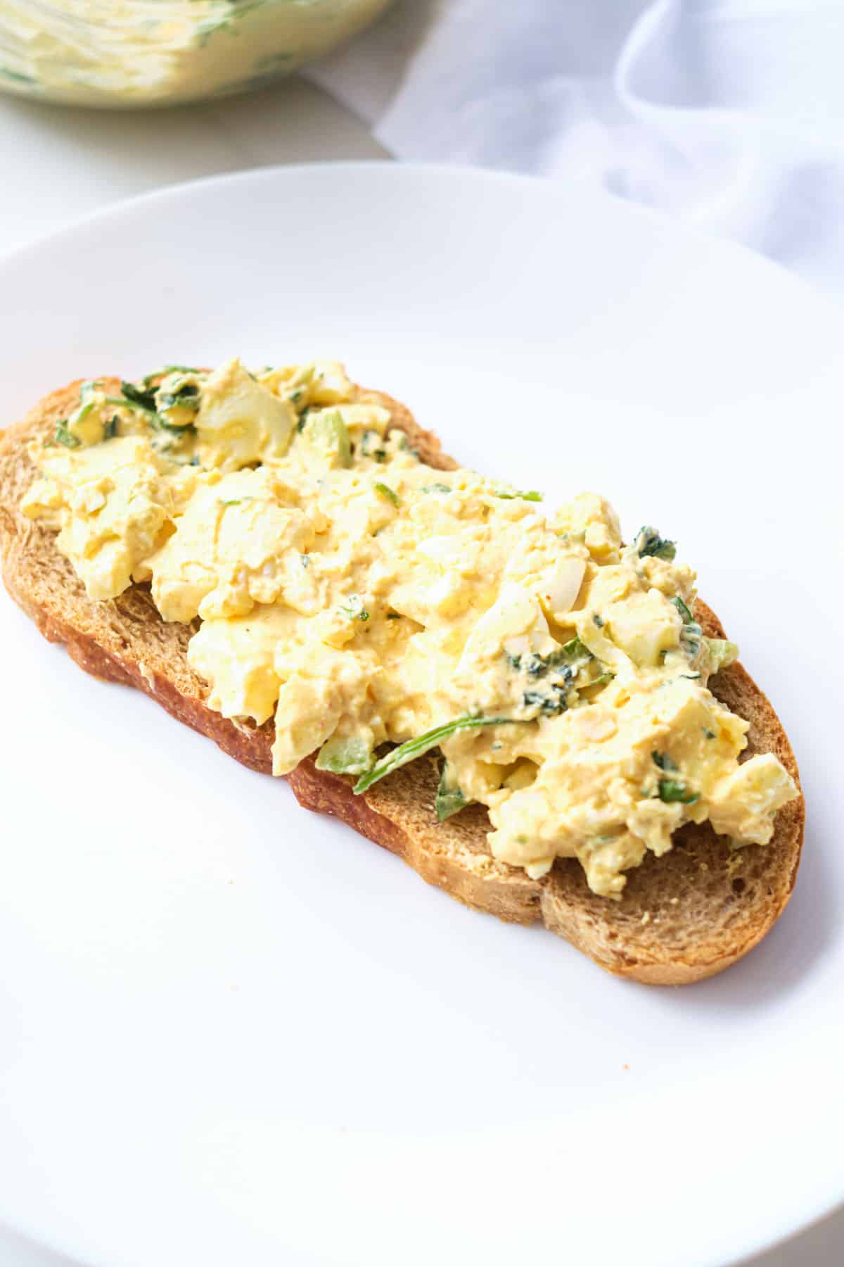 an open faced egg salad sandwich on a white plate