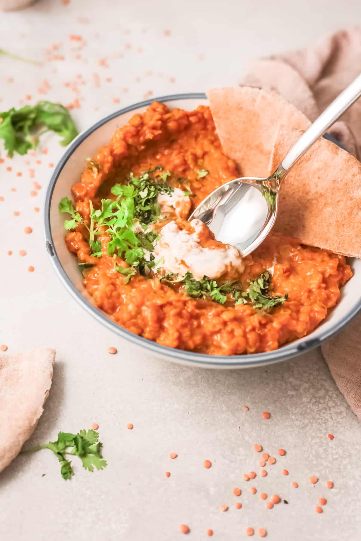a bowl of red lentil curry with a spoon removing one bite