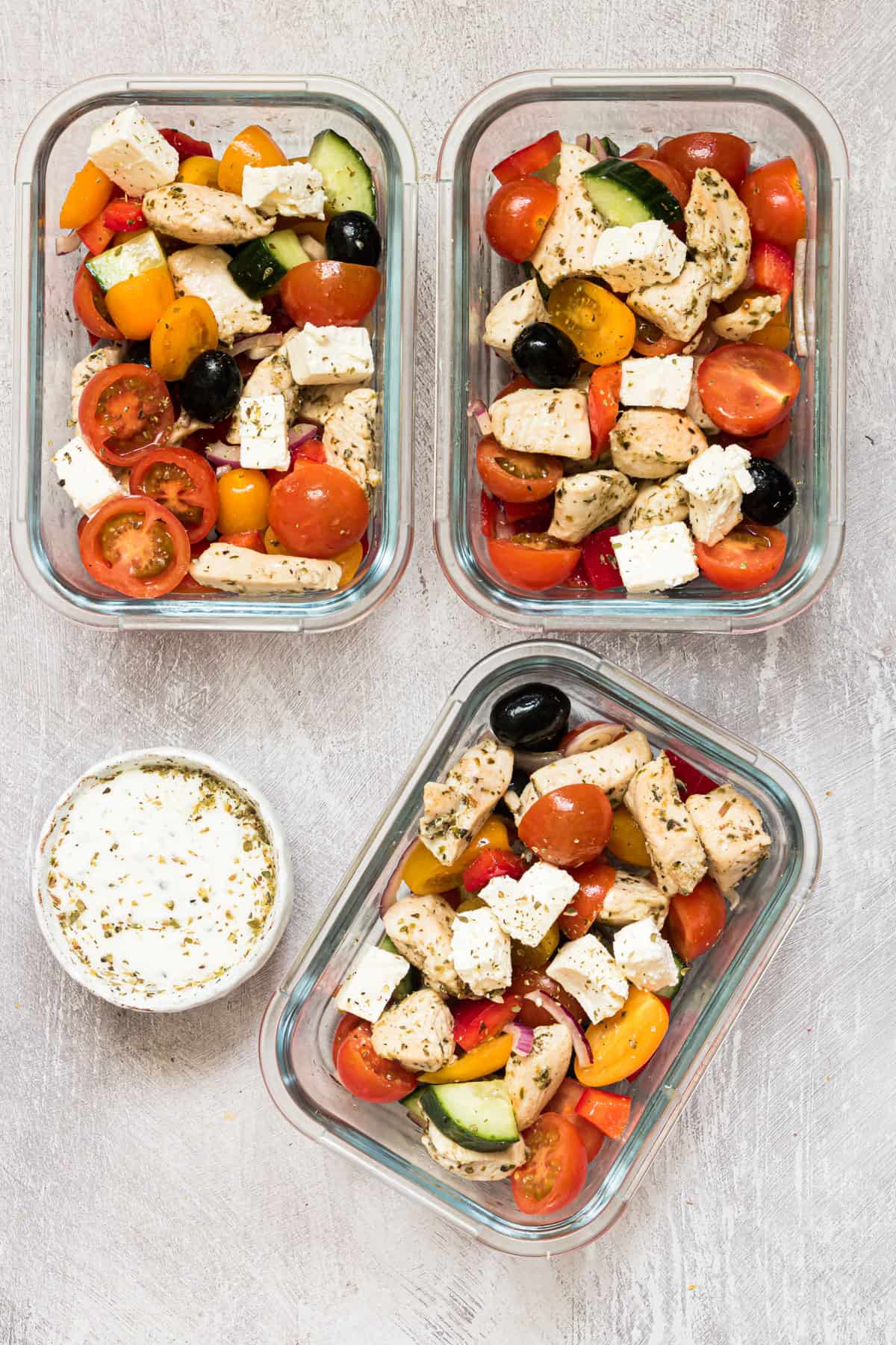 the finished greek chicken recipe in 3 meal prep containers with a dish of tzatziki sauce