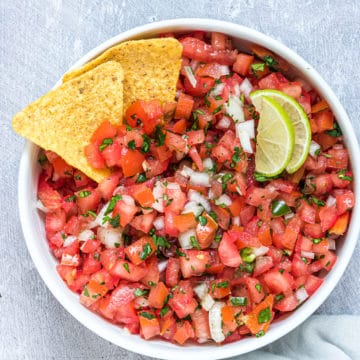 the finished pico de gallo in a serving bowl garnished with two chips and lime wedges