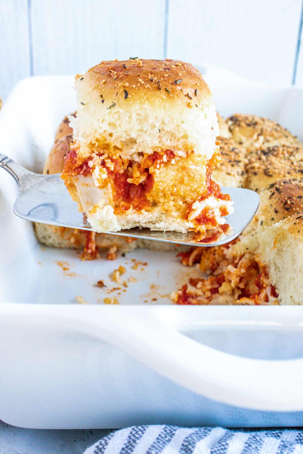 close up for parmesan chicken sliders on a serving spoon over a tray of sliders