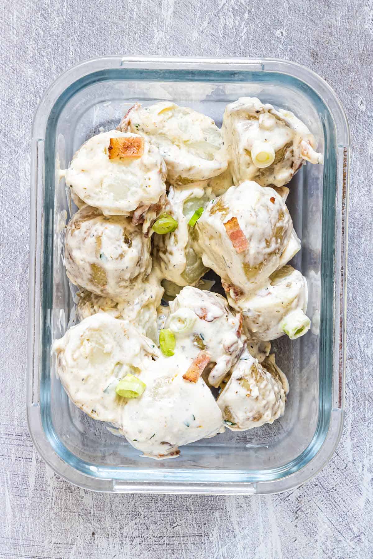 close up of loaded potato salad in a meal prep glass container