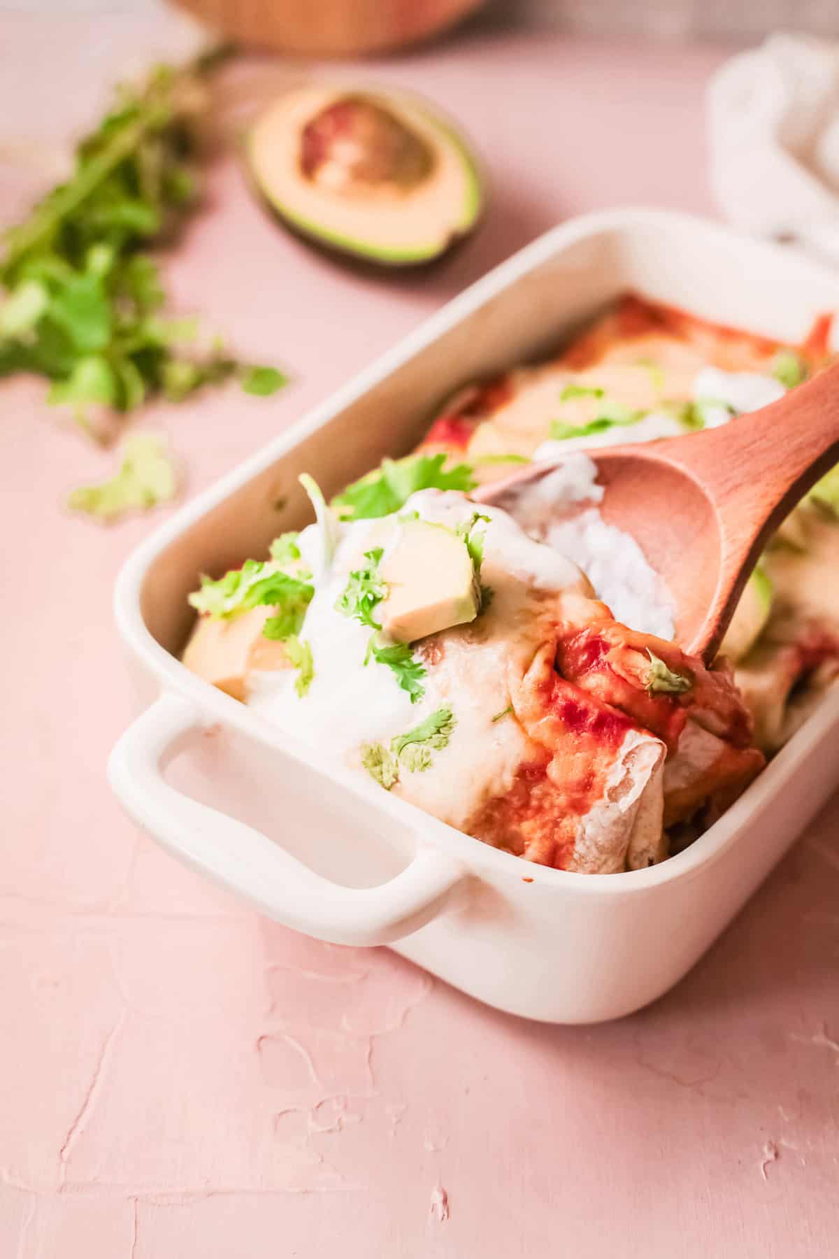 a wooden spoon scooping a portion of slow cooker chicken enchilada casserole out of the baking dish