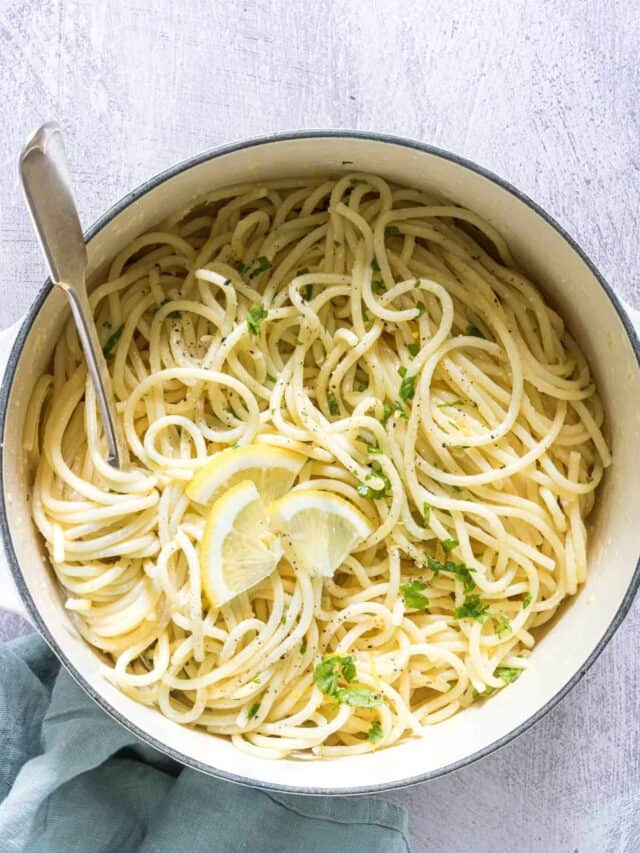 a dish of garlic butter pasta garnished with parsley and lemon wedges