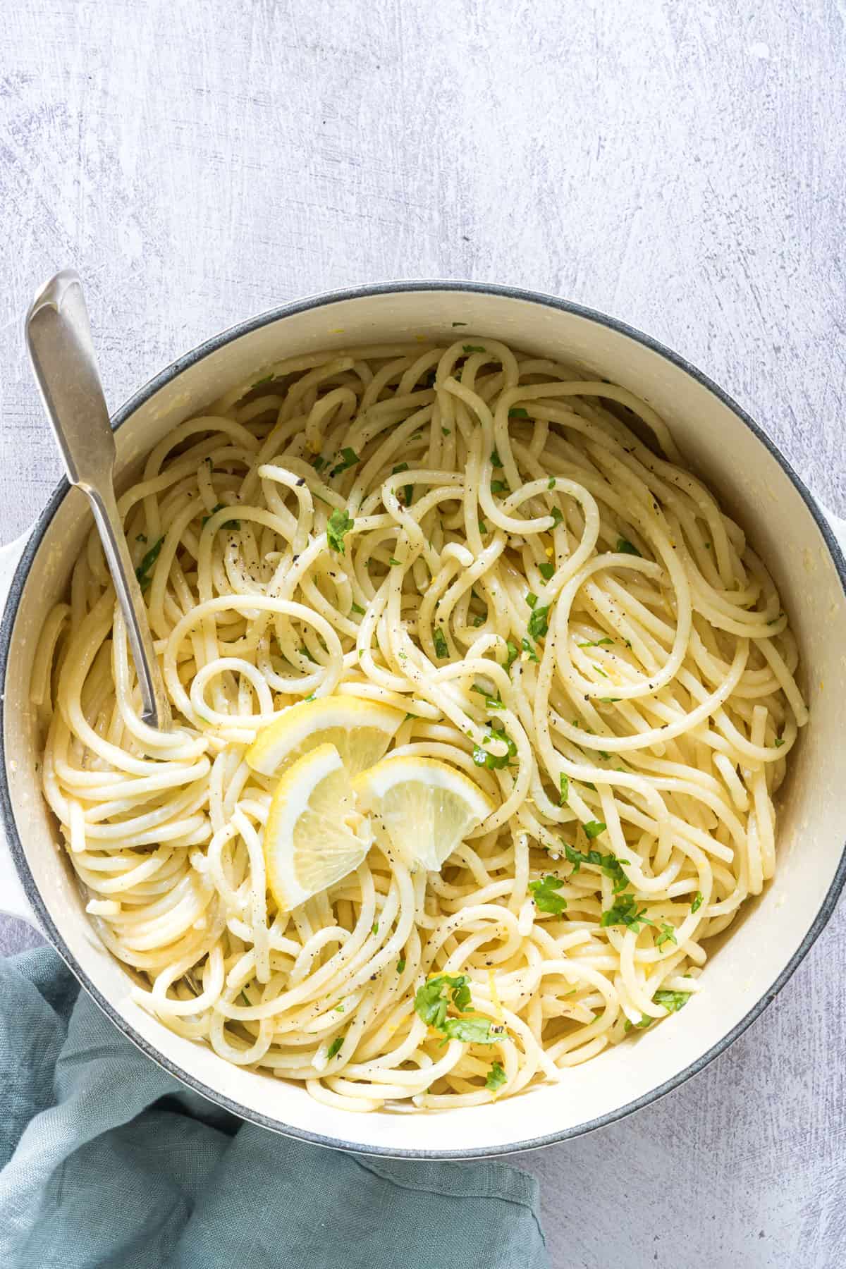 a dish of garlic butter pasta garnished with parsley and lemon wedges