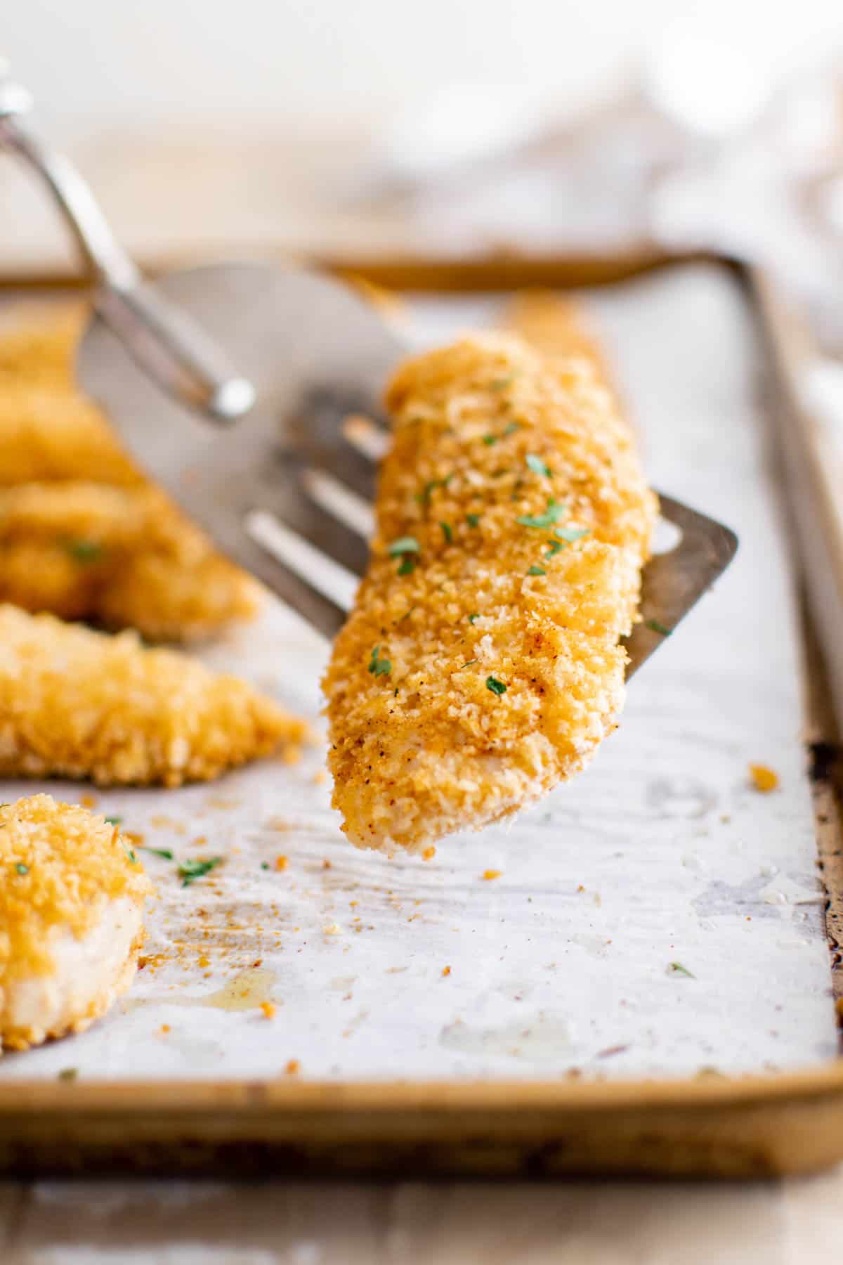 a spatula removing one of the baked chicken tenders from the pan