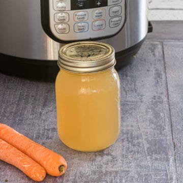 a glass jar filled with instant pot chicken stock in front of the Instant Pot