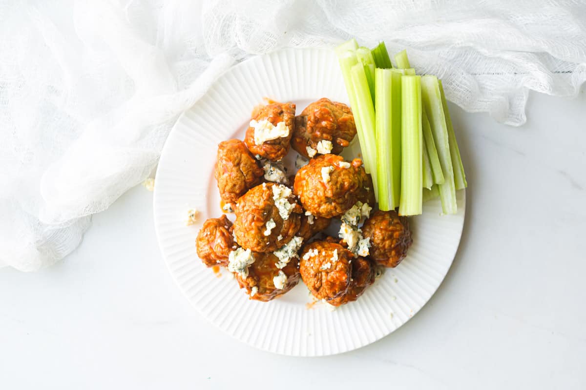top down view of a plate filled with buffalo chicken meatballs, celery sticks, and blue cheese crumbles
