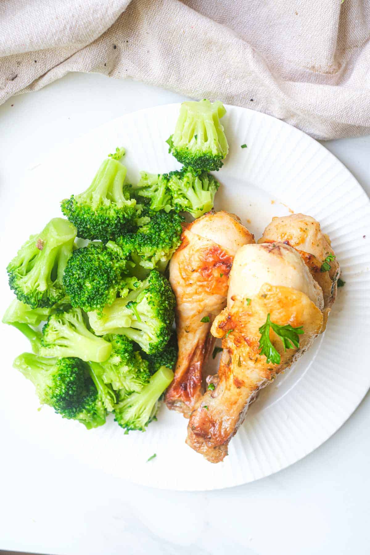 two Ranch Chicken Drumsticks on a white plate with a serving of broccoli
