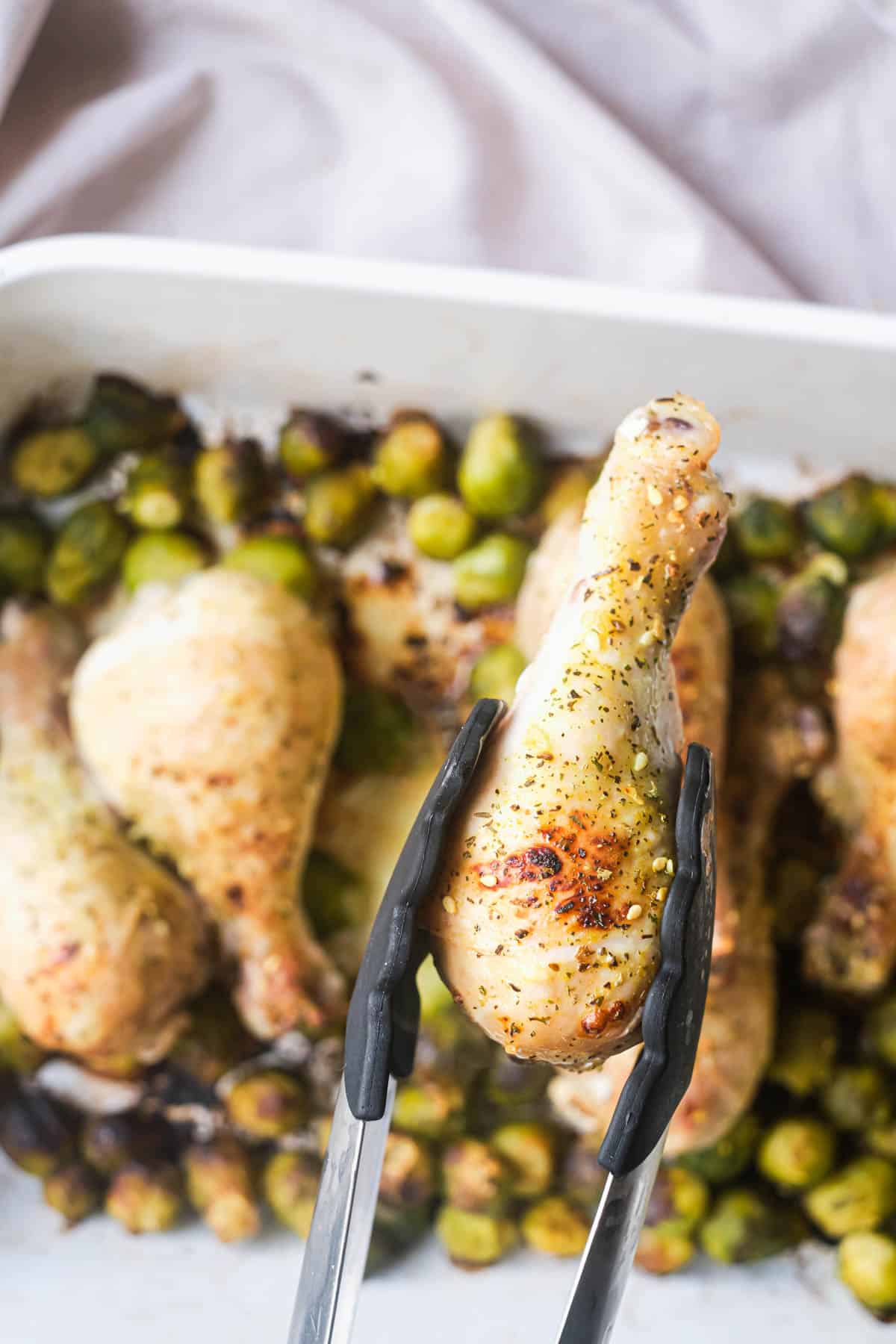 one of the lemon pepper drumsticks being removed from the baking dish with tongs