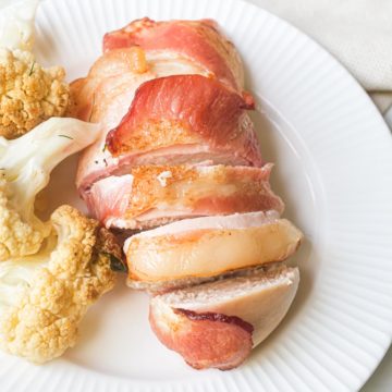 top down view of the completed bacon wrapped chicken in air fryer served on a white plate with cauliflower