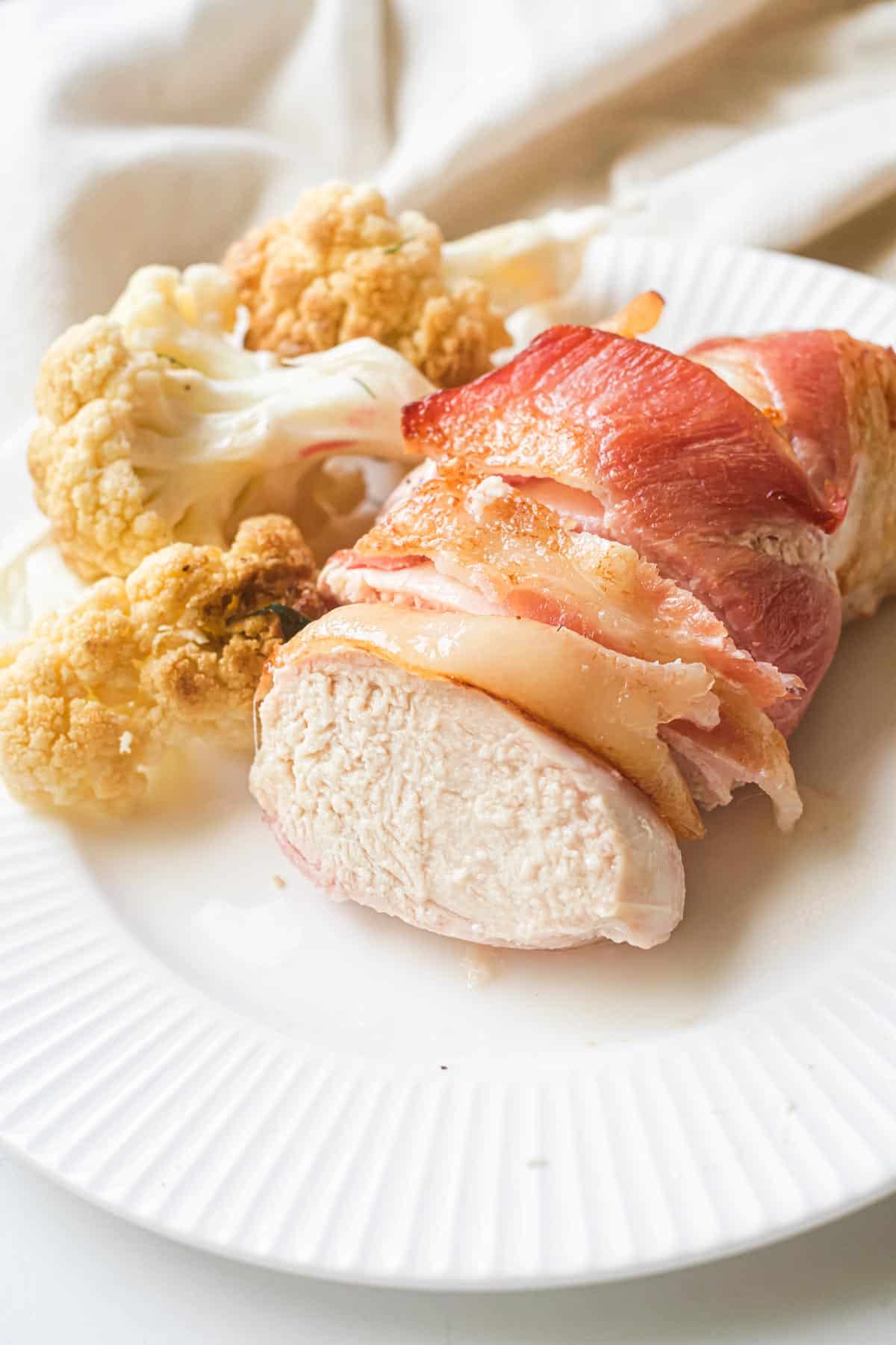 the finished air fryer bacon wrapped chicken breast served on a white dinner plate