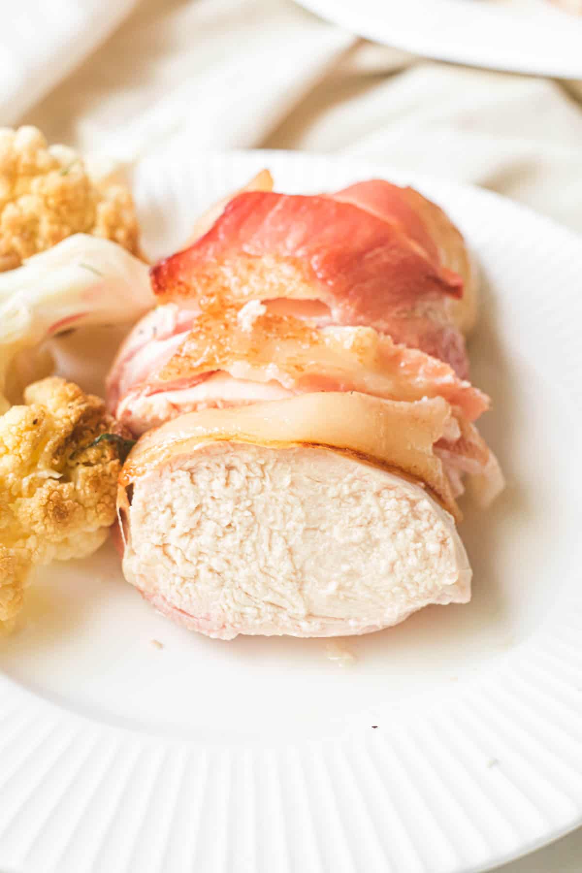 close up view of one portion of bacon wrapped chicken in air fryer on a white plate