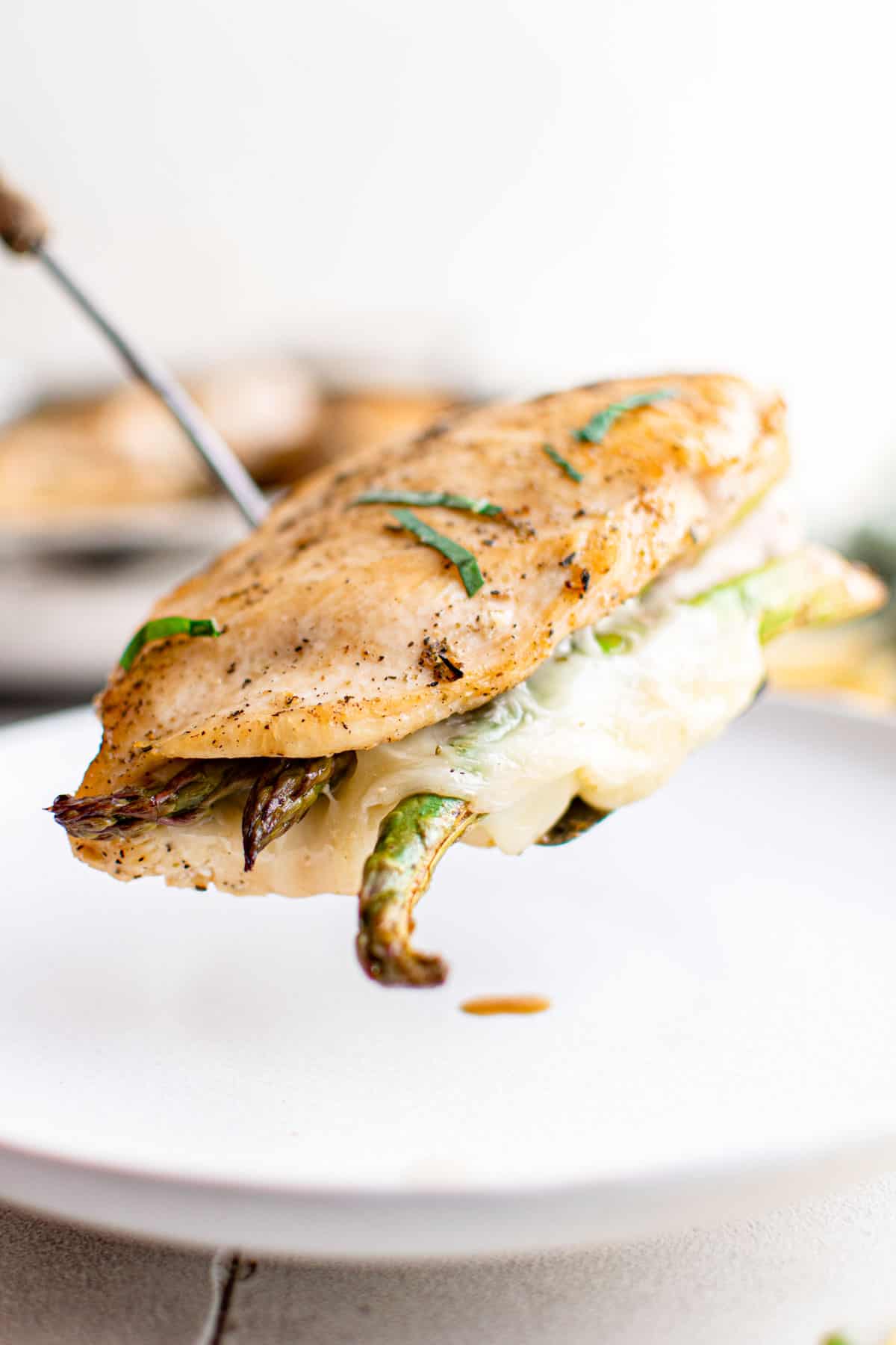 a spatula removing one cooked asparagus stuffed chicken breast from the skillet
