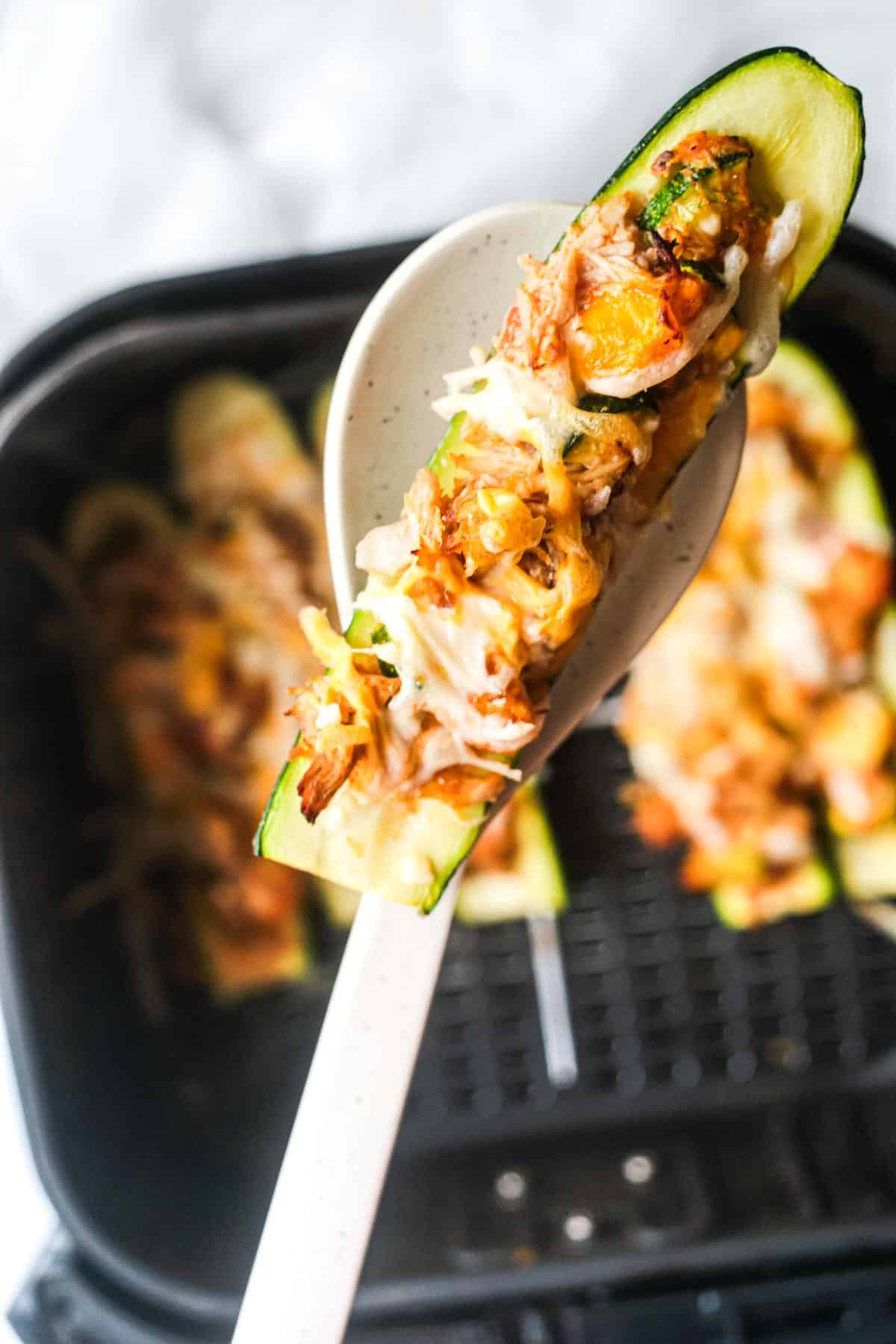 a spoon removing one of the buffalo chicken zucchini boats from the air fryer basket