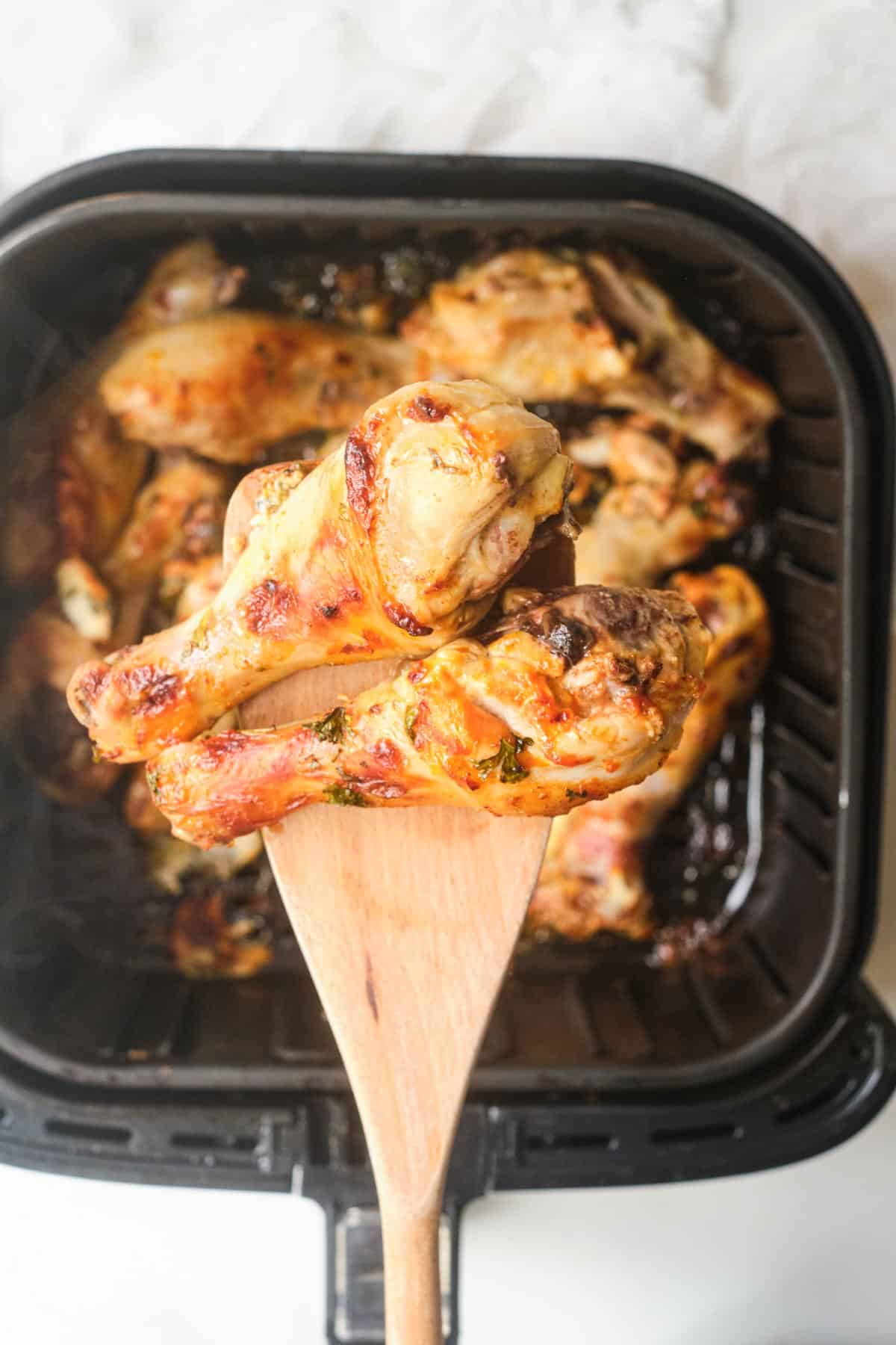 a wooden spoon removing two of the finished buffalo drumsticks from the air fryer