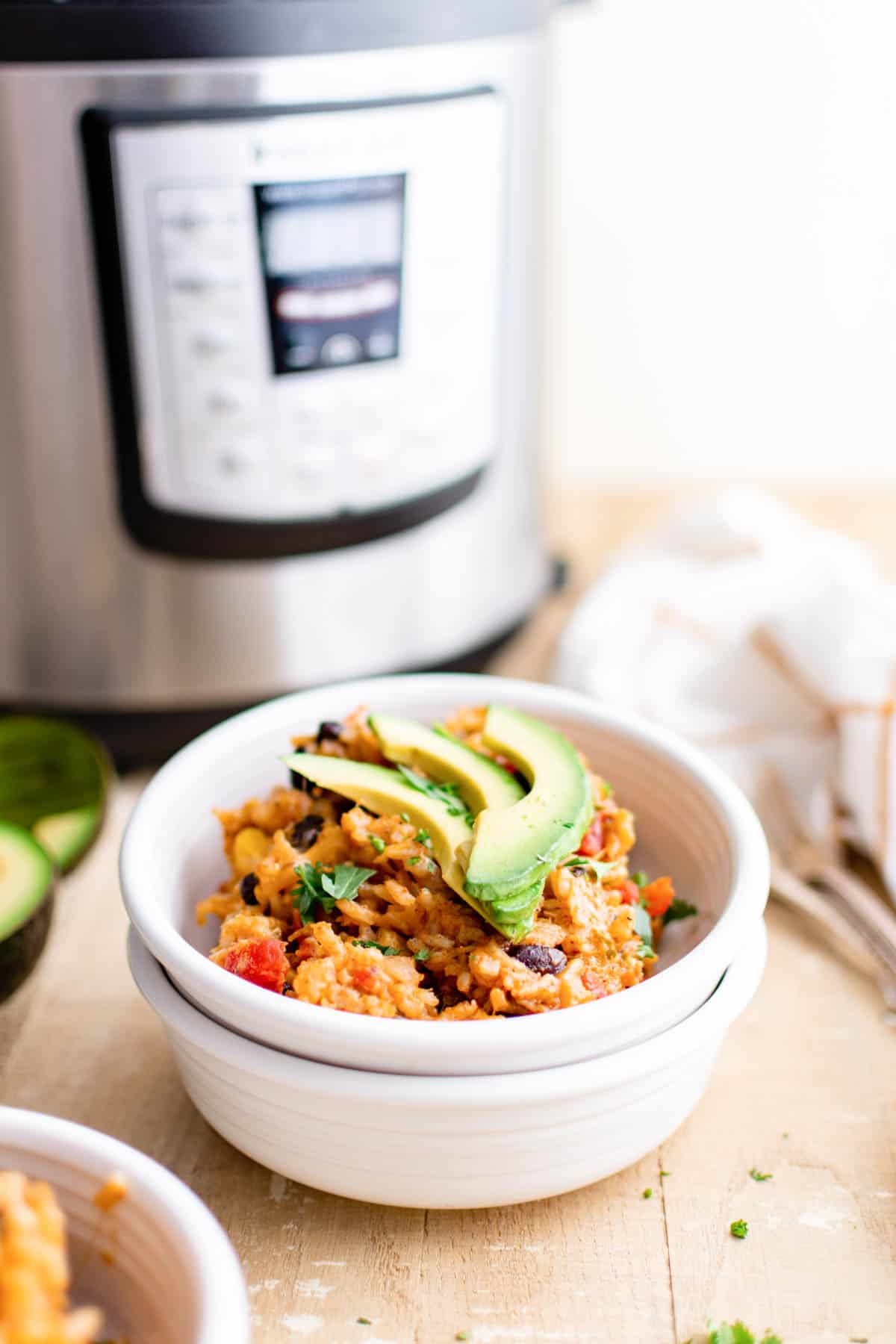 a serving of instant pot enchilada rice in a white bowl in set in front of the instant pot.