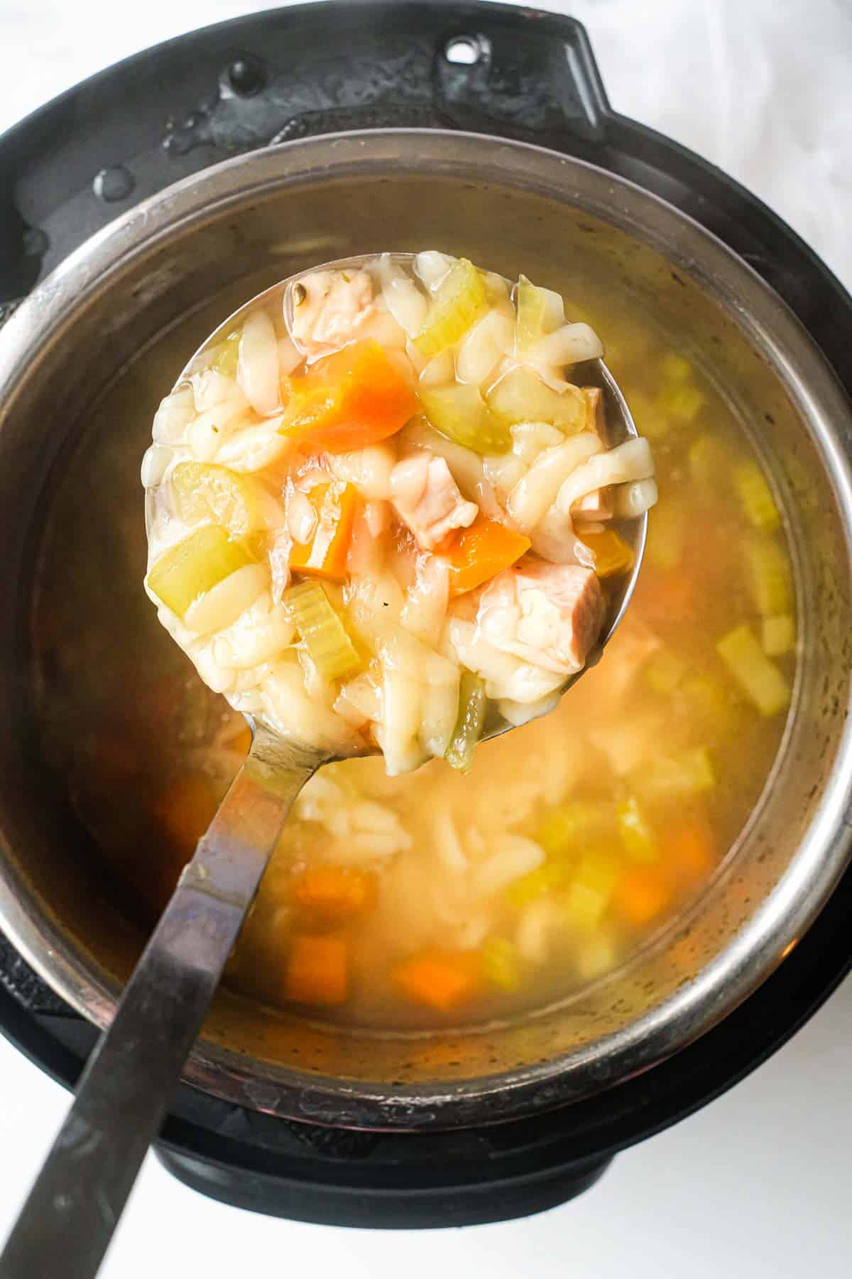 top down view of the completed instant pot lemon chicken orzo soup inside the instant pot with a ladle removing one scoop