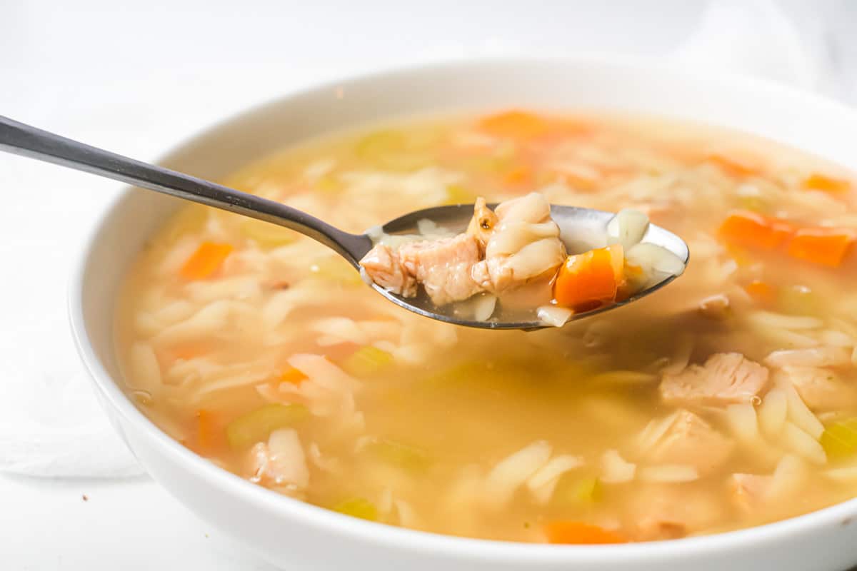 profile view of a spoon removing one bite of instant pot lemon chicken orzo soup from a white bowl