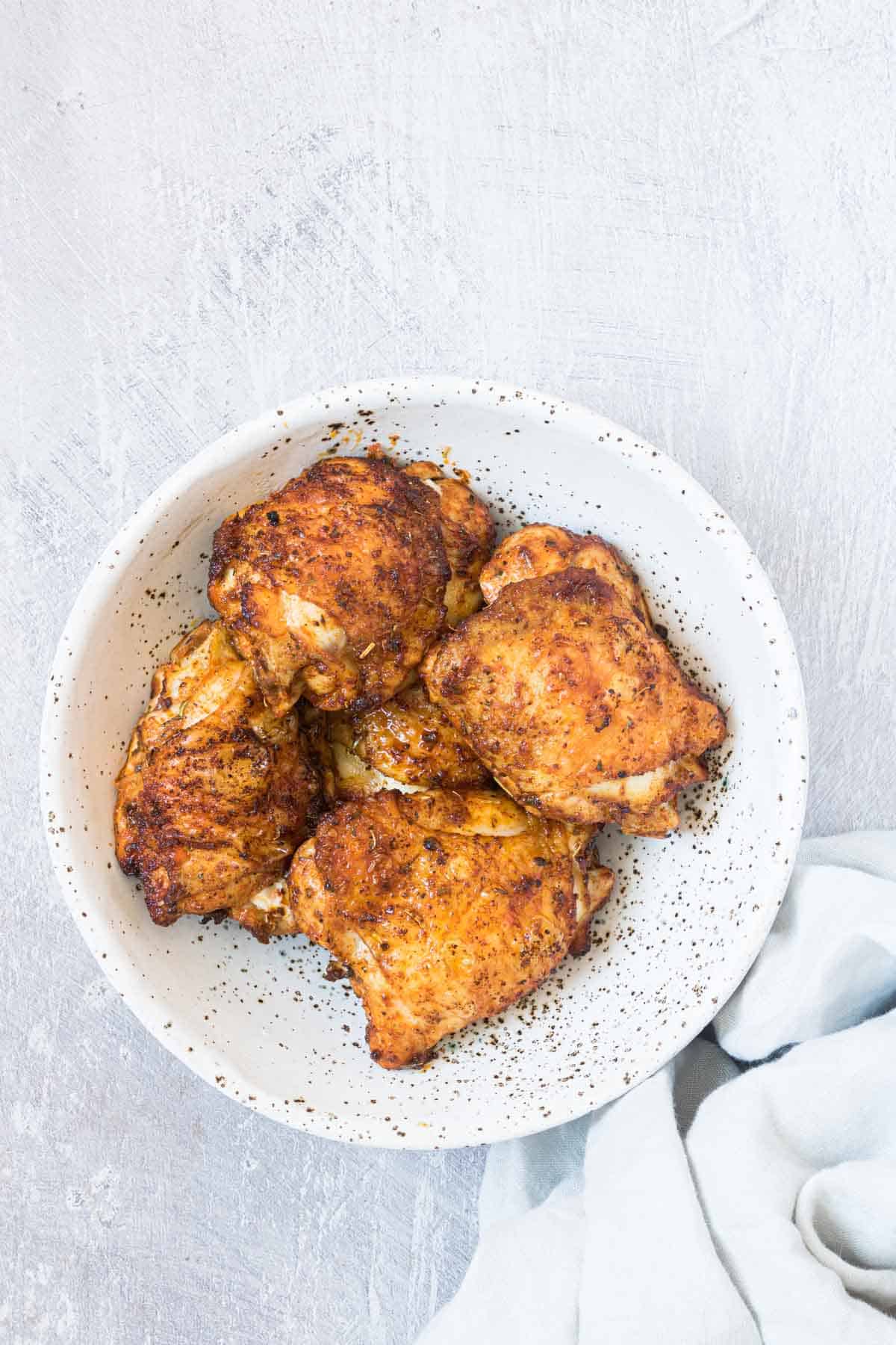 top down view of the completed air fryer chicken thighs in a white bowl with cloth napkin
