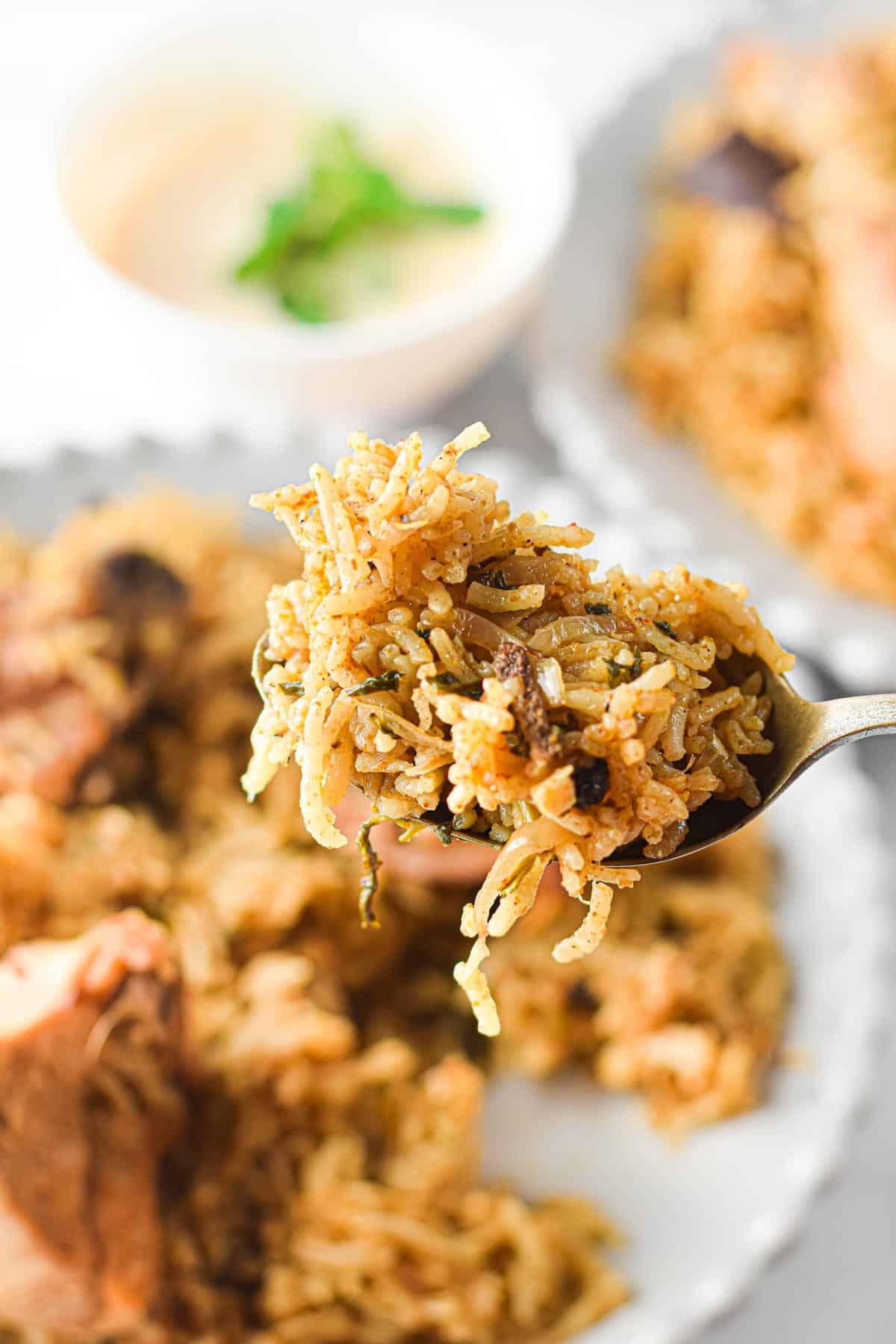 a spoon removing one bite of instant pot chicken biryani from a white dinner plate