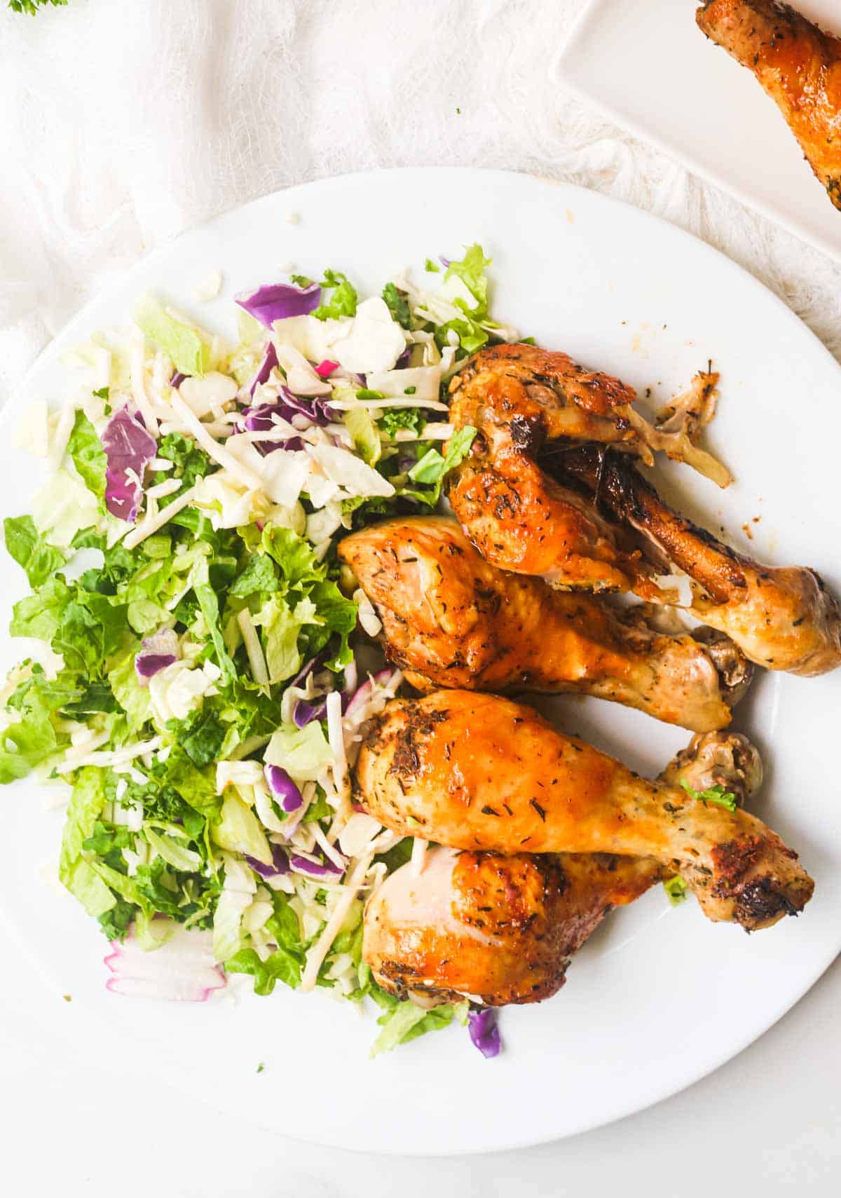 top down view of a serving of instant pot chicken drumsticks on a white plate with a green salad