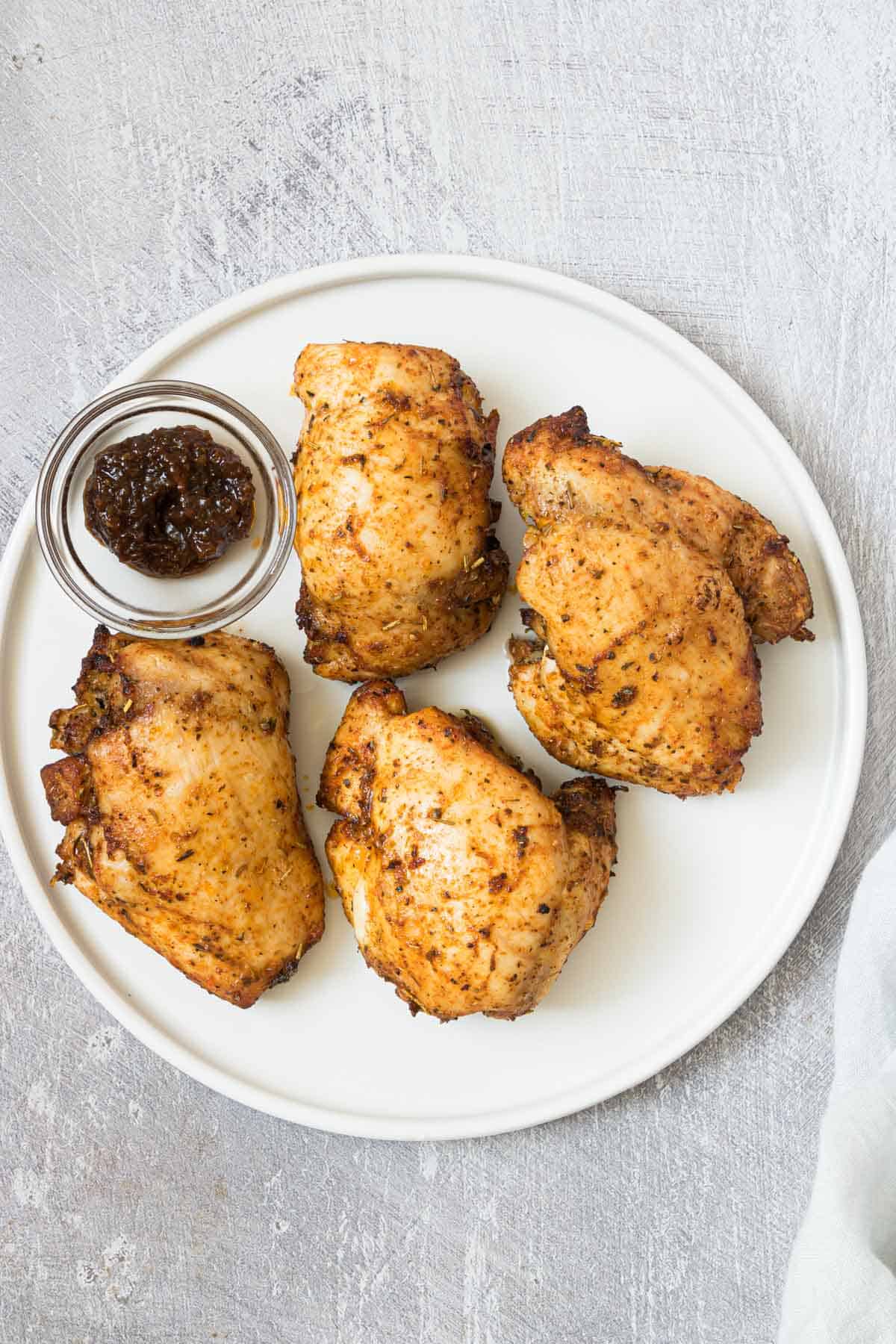 air fryer boneless chicken thighs served on a white plate with extra cup of marinade