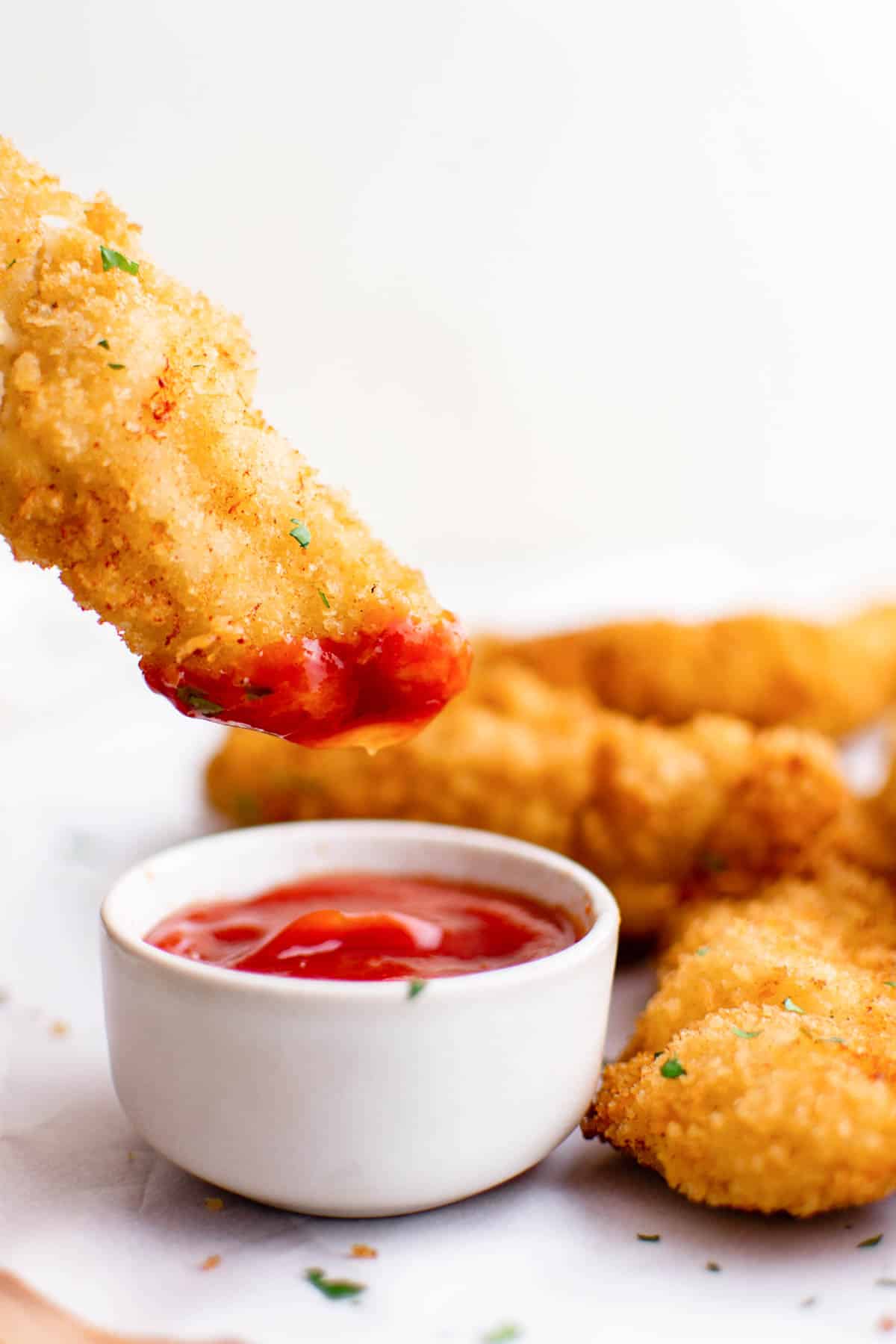 close up view of air fryer chicken tenders being dipped in ketchup