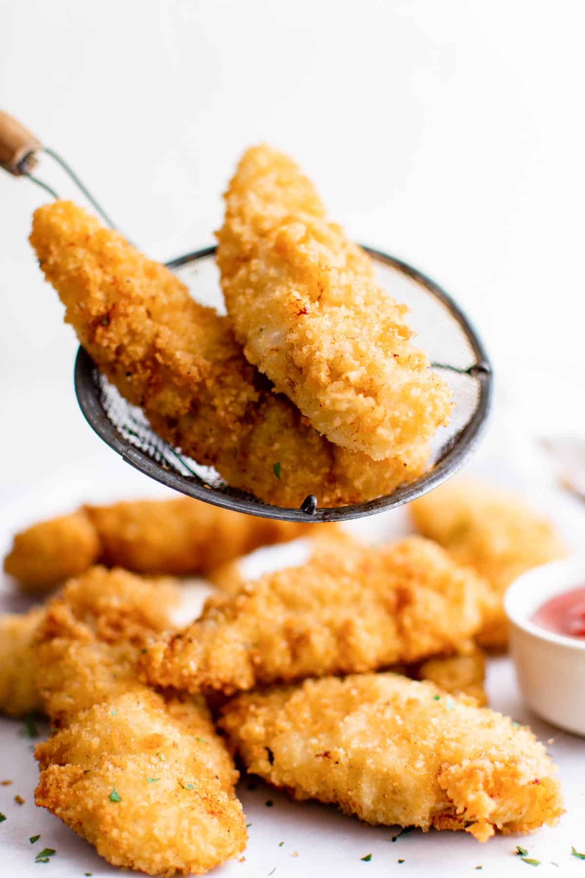 a serving utensil placing two air fryer chicken tenders onto a serving platter