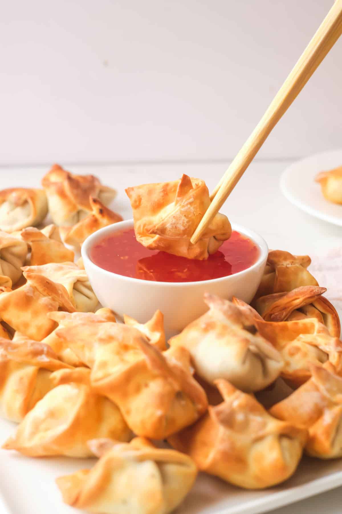 one wonton held by chopsticks and being dipped into sauce