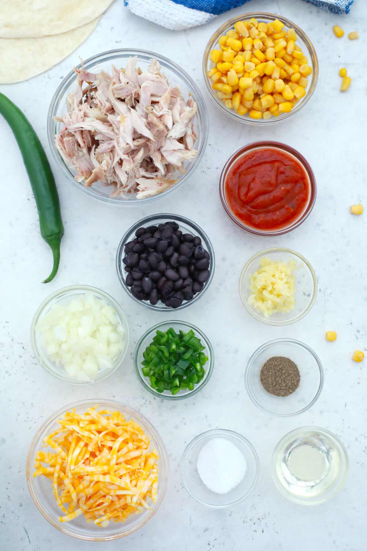 ingredients for making air fryer chicken taquitos on a tables with chicken, cheese, black. beans, peppers and more.