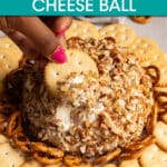 A close up of a hand dipping a cracker in a cheese ball.