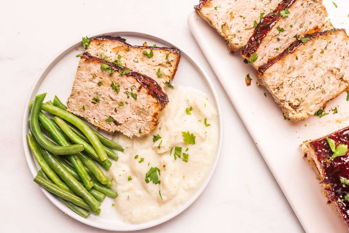 top down view of a serving of chicken meatloaf with potatoes and green beans on a white plate