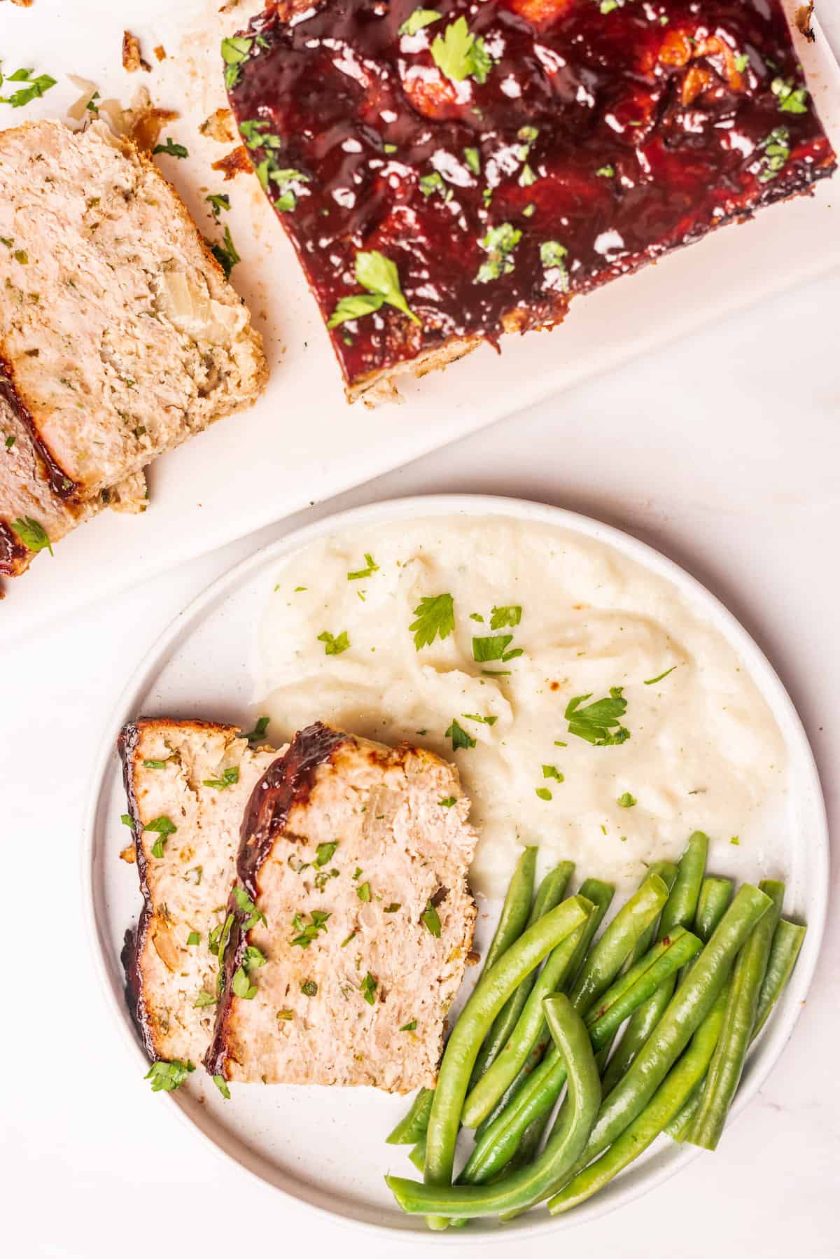 top down view of a serving of chicken meatloaf on a plate with mashed potatoes and green beans