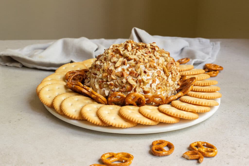 side view of the cheeseball on a platter surrounded by crackers and pretzels