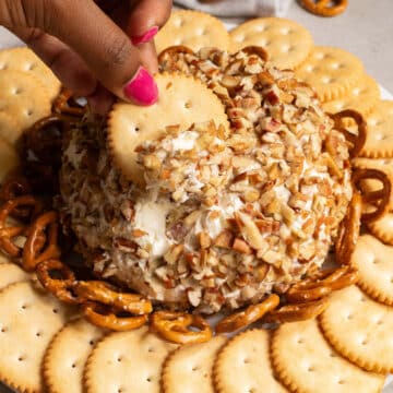 a hand dipping one cracker into the cheese ball