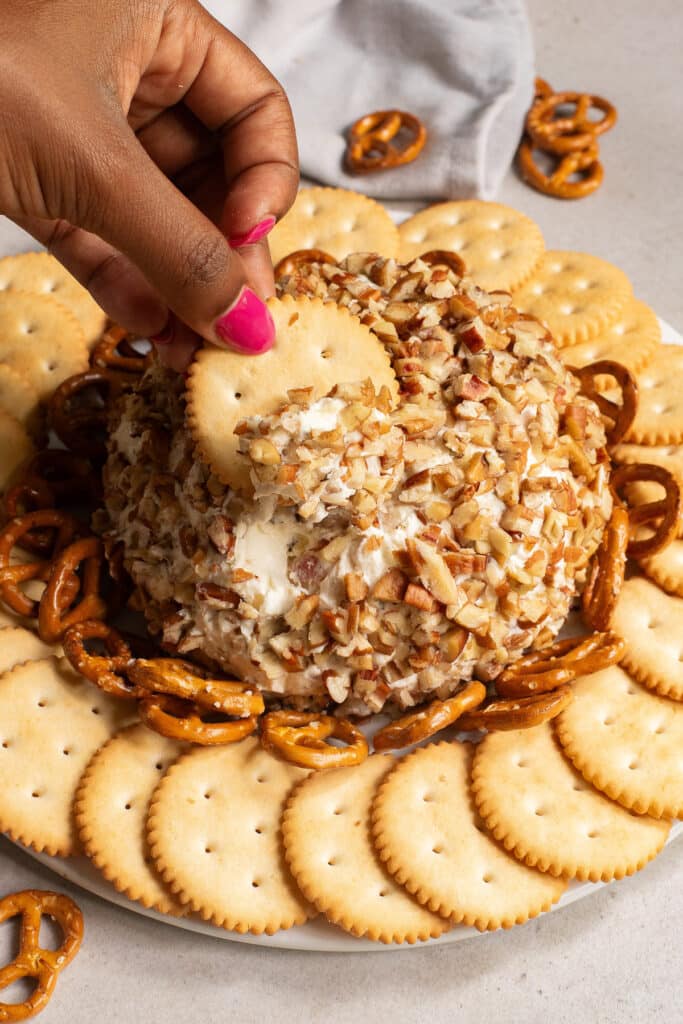 a hand dipping one cracker into the cheese ball
