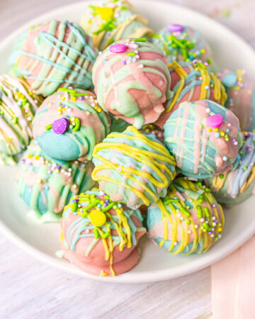 A plate of Easter-themed Oreo truffles in pastel hues, coated with smooth chocolate and topped with vibrant drizzles, sprinkles, and small sugar decorations.