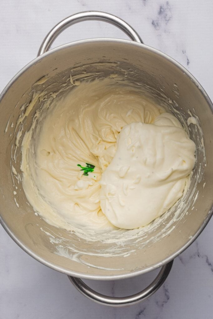 green food coloring being added to the combined dip ingredients.