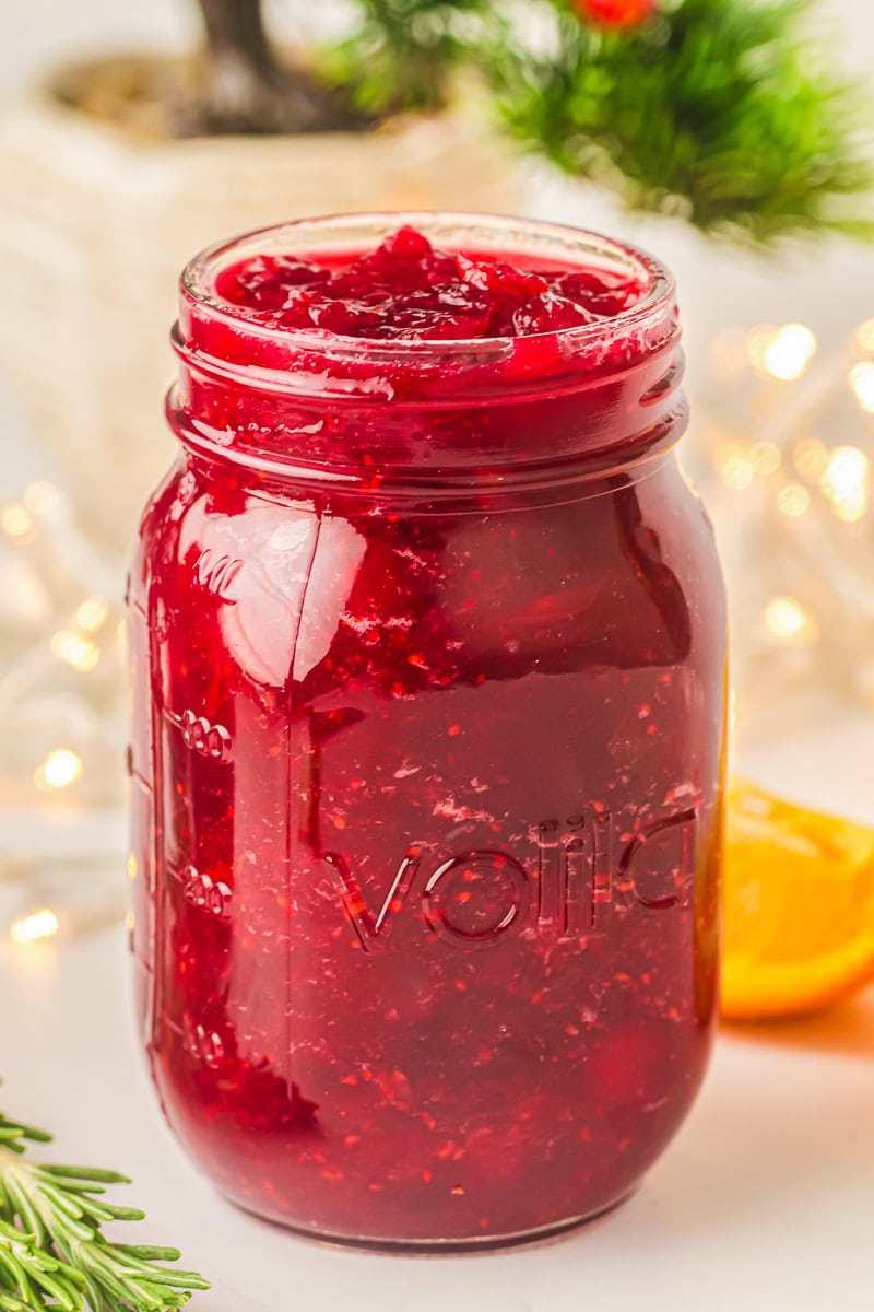 Close-up of homemade orange cranberry sauce in a glass jar, showing a rich, glossy red color and chunky texture.